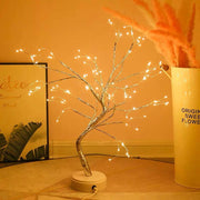 Decorative LED tree with lights on a wooden surface, next to a cylindrical container with text.
