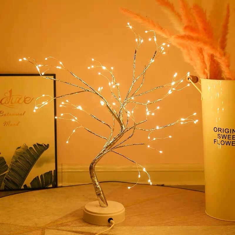Decorative LED tree with lights on a wooden surface, next to a cylindrical container with text.