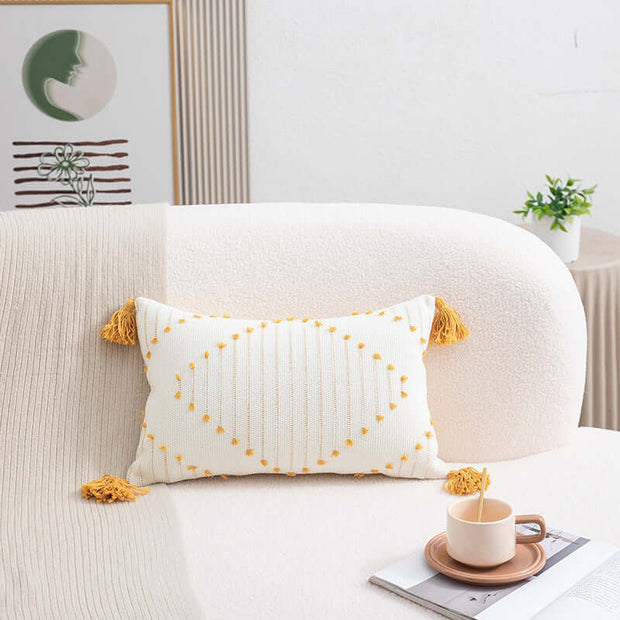 Decorative pillow with yellow tassels on a sofa with a cup and saucer in a cozy living room.