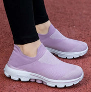 Purple slip-on shoes worn with black pants on a red surface