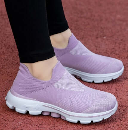 Purple slip-on shoes worn with black pants on a red surface