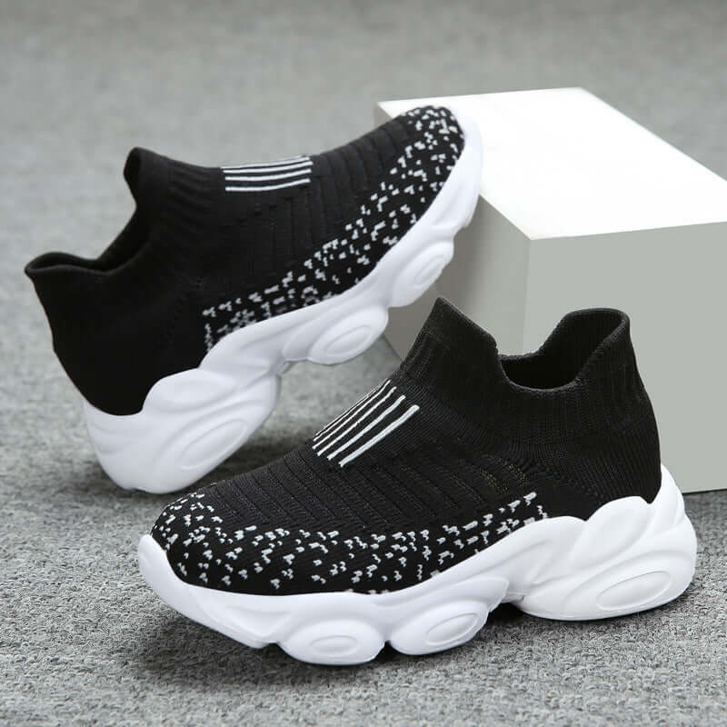 Black and white sock sneakers on a gray surface with a white block background