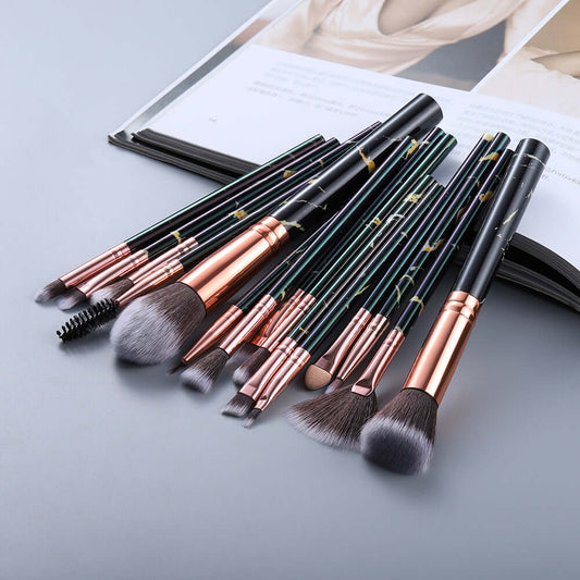 Set of makeup brushes with black and rose gold handles on a light gray surface.