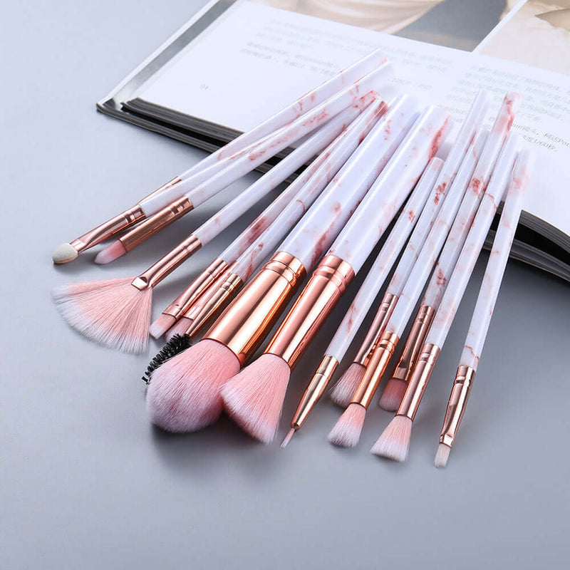 Set of makeup brushes with rose gold and white handles on a light gray surface.