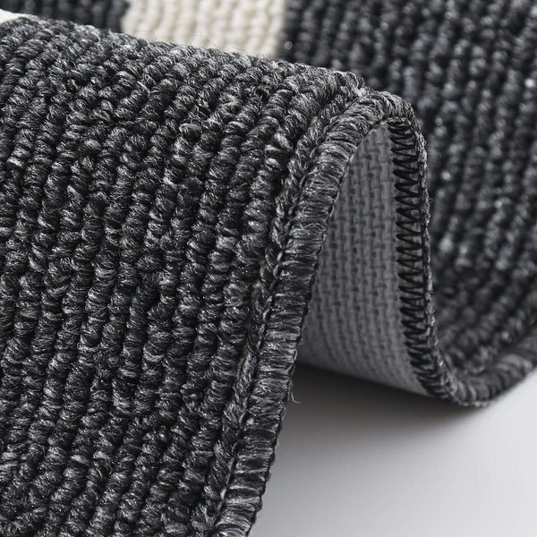 Close-up of a textured black and gray rug corner on a light background