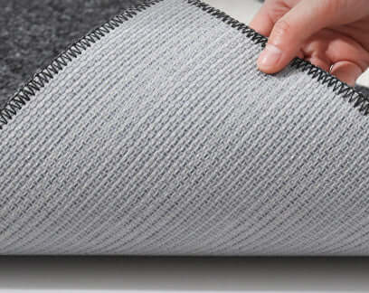 Person rolling out a gray rug on a light-colored floor