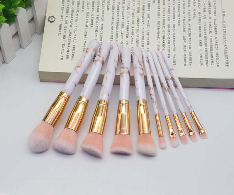 Set of makeup brushes with marble handles on a white surface