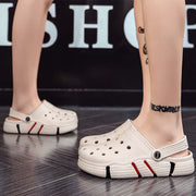 White clogs with red and black accents worn by a person on a dark floor.