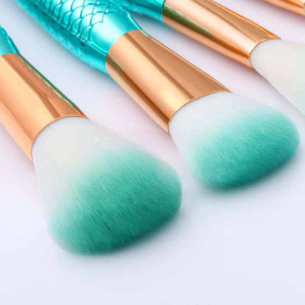 Makeup brushes with gradient green bristles and gold handles on a light background