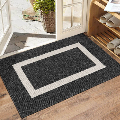 Black doormat with a white border on a wooden floor, leading to a glass door.