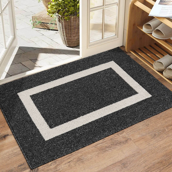 Black doormat with a white border on a wooden floor, leading to a glass door.