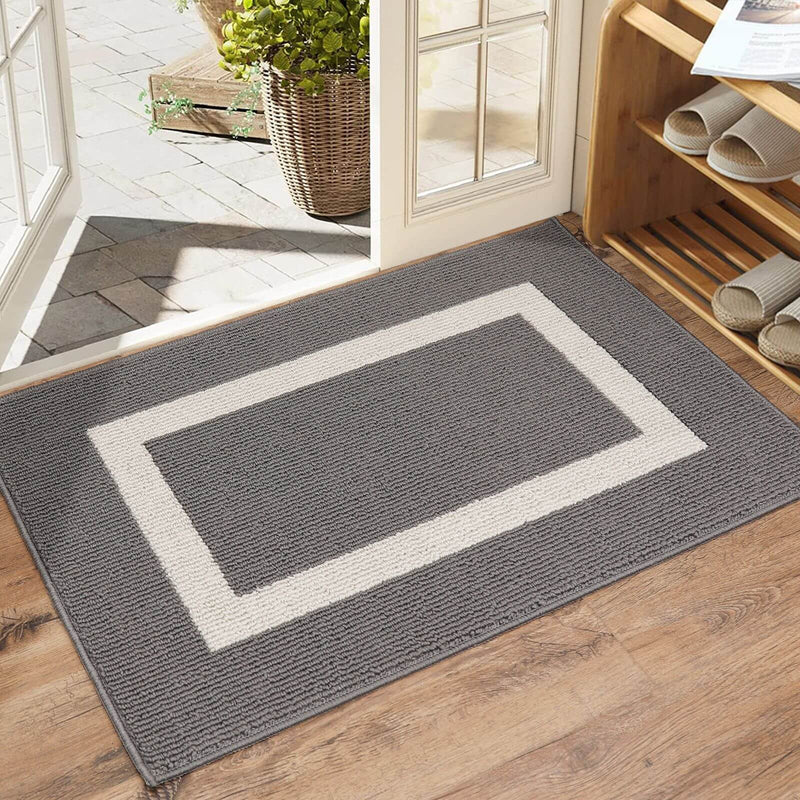 Gray doormat with white border on wooden floor, leading to a glass door.