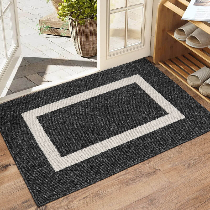 Black doormat with a white border on a wooden floor, leading to a glass door.