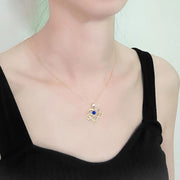 Person wearing a gold necklace with a blue pendant on a plain background