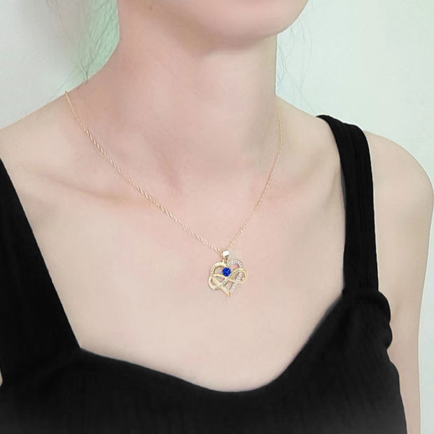 Person wearing a gold necklace with a blue pendant on a plain background