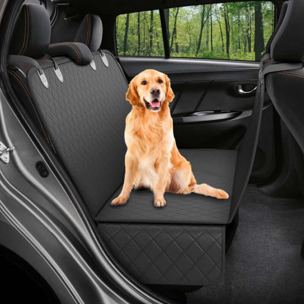 Dog sitting on a black car seat cover inside a vehicle with trees outside.