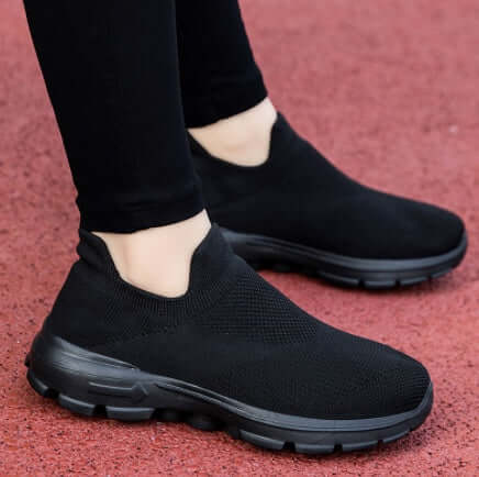 Black slip-on shoes worn with black pants on a red surface