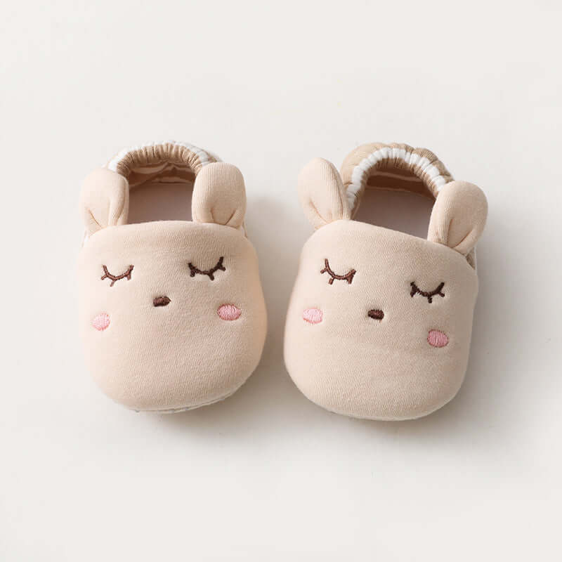 Pair of beige baby slippers with cute face designs on a light background