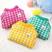 Three colorful checkered pet sweaters on a light background