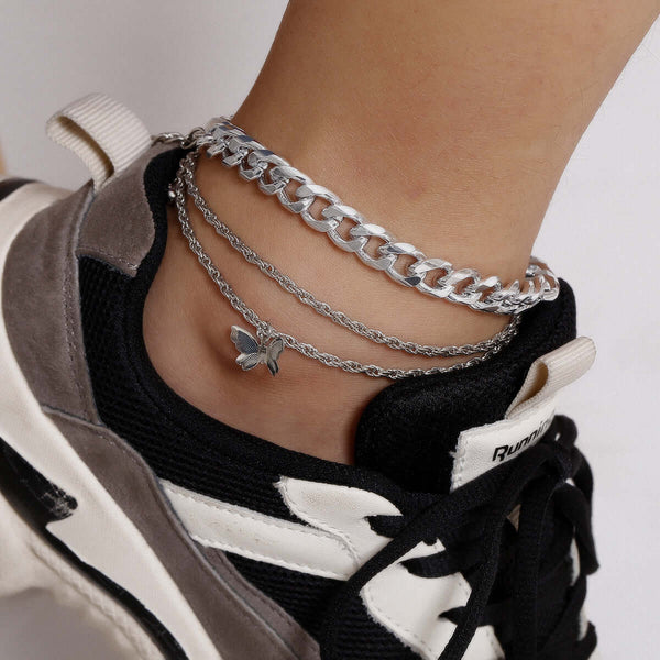 Silver chain anklets with a butterfly charm on a person wearing black and white sneakers.