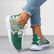 Green sneakers with white patterns worn by a person on a light background