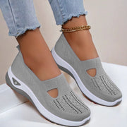 Gray slip-on shoes with white soles worn with light blue jeans on a neutral background