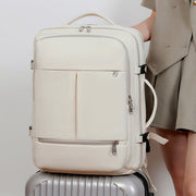 Beige backpack on a silver suitcase with a person wearing a beige outfit in the background