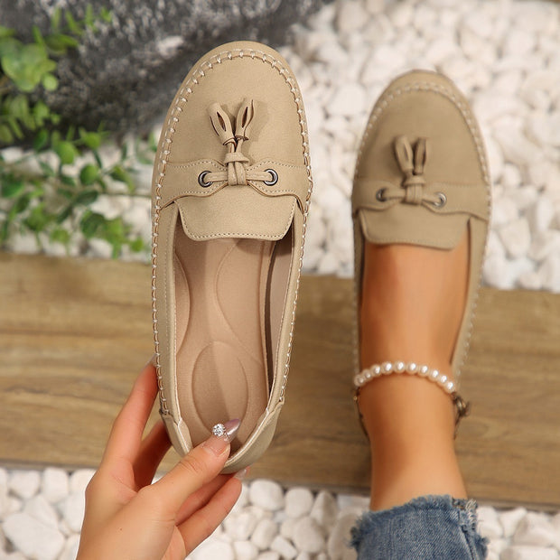 Beige loafers with tassels held by a hand on a blurred natural background