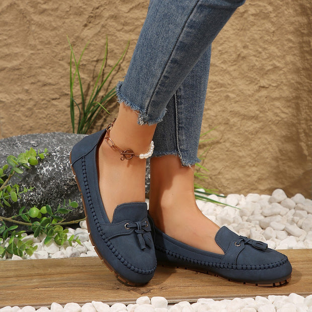 Navy loafers worn with ripped jeans against a natural stone background