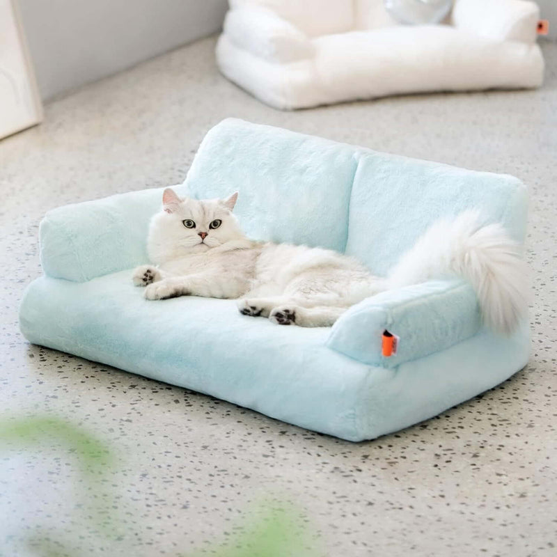 Light blue pet bed with a white cat lying on it, on a speckled countertop.