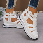 White sandals with black soles worn by a person on a neutral background