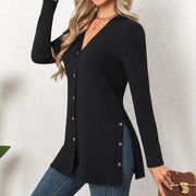 Person wearing a black cardigan with gold buttons on a neutral background