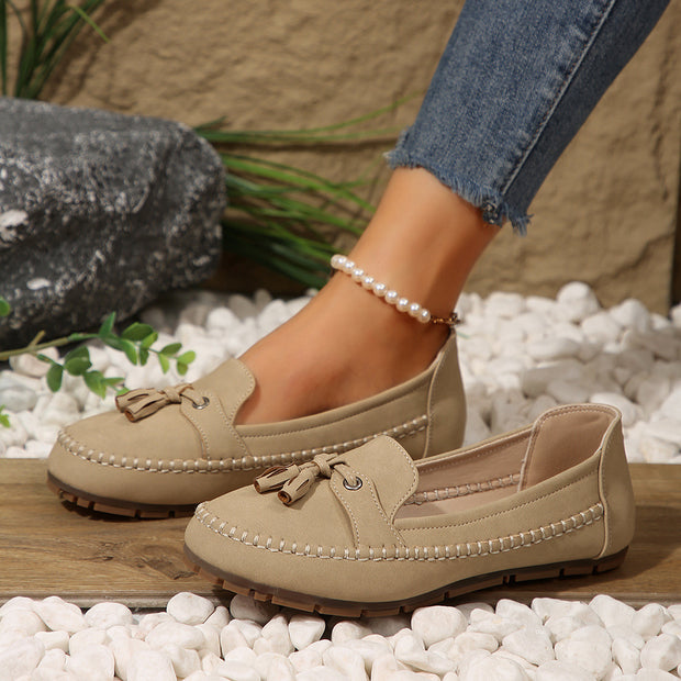 Beige loafers worn with jeans on a pebbled surface.