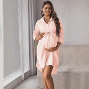 Pregnant woman wearing a pink striped dress in a room with a couch and curtains.