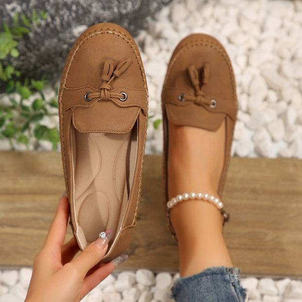 Brown loafers with tassels held by a hand against a blurred natural background