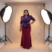 Woman wearing a blue and red outfit with a peplum top and burgundy skirt, posing in front of a door.