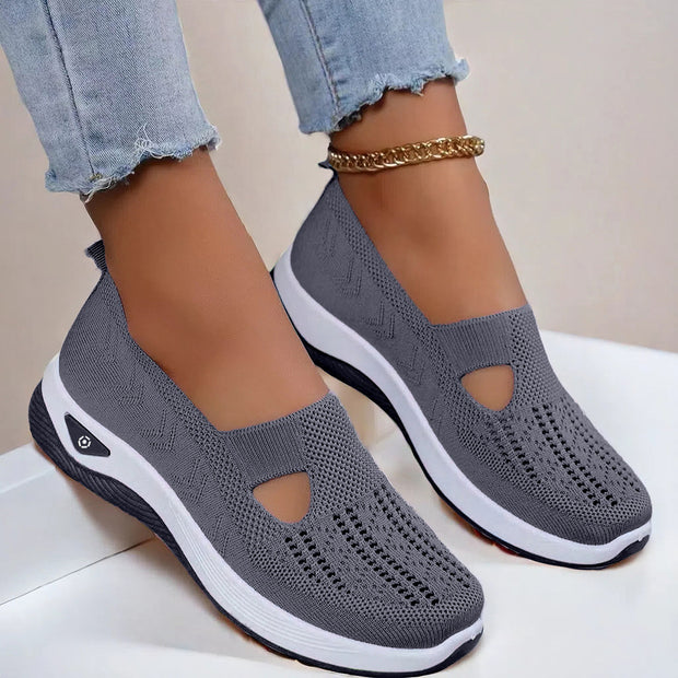 Gray slip-on shoes with white soles worn with light blue jeans on a neutral background