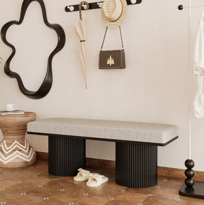 Bench with textured seat and black legs in a room with a mirror, shoes, and decorative items.
