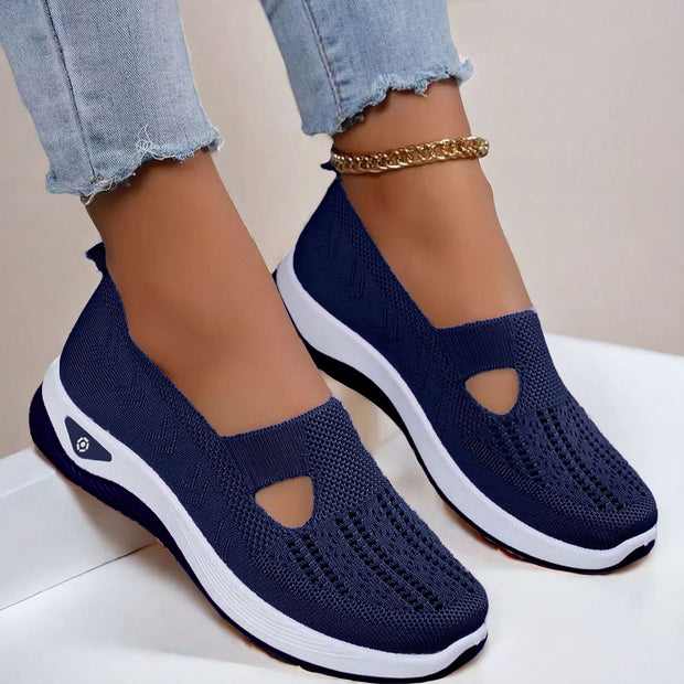 Navy slip-on shoes with white soles worn with light blue jeans on a neutral background