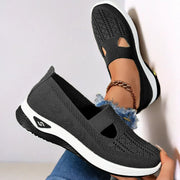 Black slip-on shoes with white soles worn by a person on a light gray background