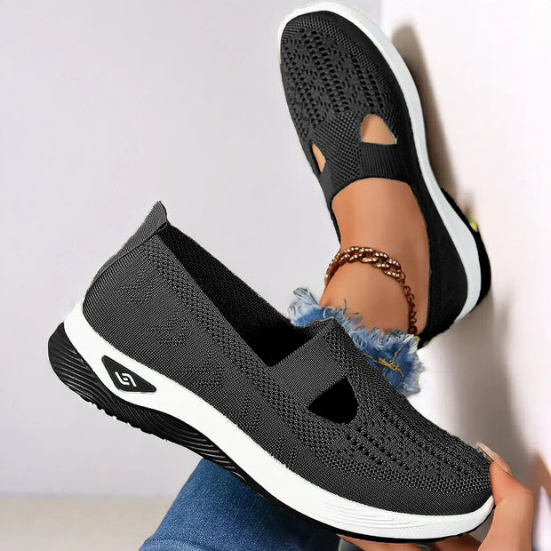 Black slip-on shoes with white soles worn by a person on a light gray background