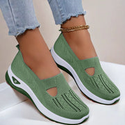 Green slip-on shoes with white soles worn by a person on a light background