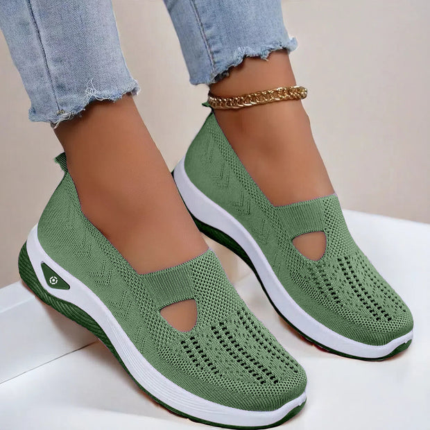 Green slip-on shoes with white soles worn by a person on a light background