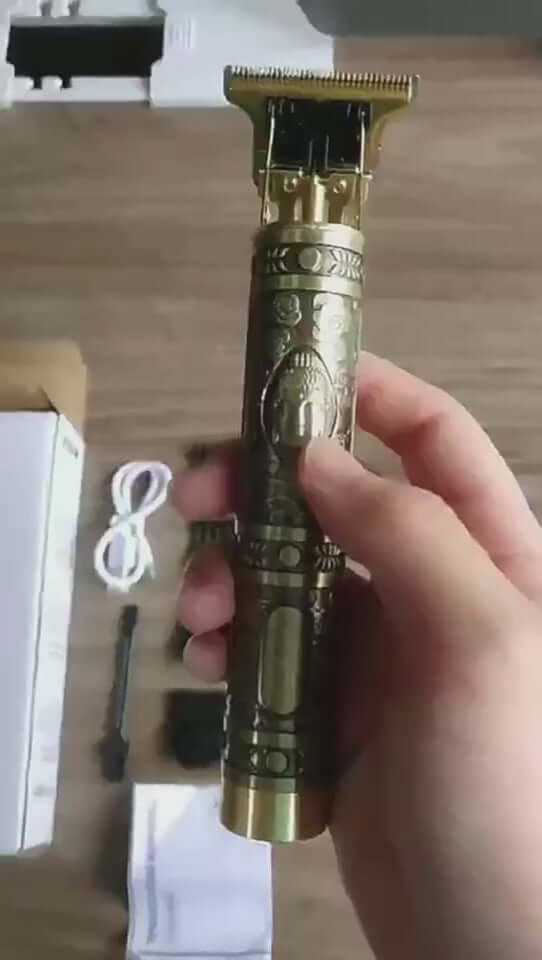 Hand holding a rechargeable USB electric hair clipper with intricate gold design, showcasing the professional trimmer features.