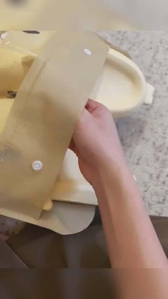 Hand adjusting the strap of a beige indoor slipper on a surface, showcasing its design and fastenings.