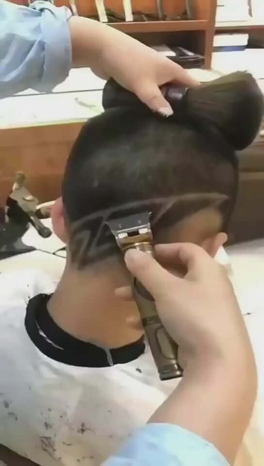 Close-up of a barber using rechargeable electric clippers on a client's hairstyle during a professional haircut.