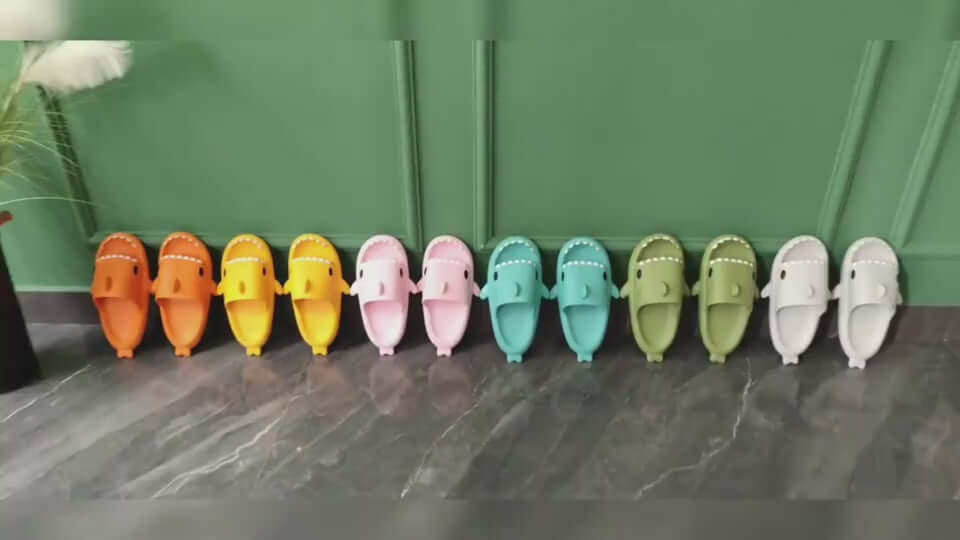 Colorful collection of cartoon shark slippers in orange, yellow, pink, green, blue, and white, lined up on a stylish floor.